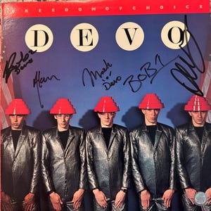 以下が含まれることがあります： バンドDevoのアルバムカバー。大きな白い文字で「DEVO」と書かれています。バンドメンバーは銀色のジャケットと赤い帽子を着用しています。背景は青色で、赤と白のストライプが入っています。