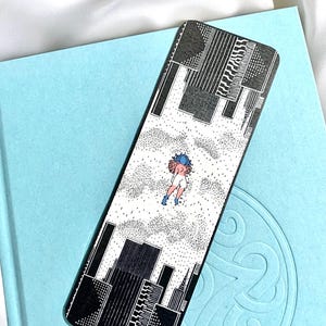 Könnte beinhalten: Schwarz-weißes Lesezeichen mit einer Skyline und einer Person im Himmel. Die Person trägt ein blaues Hemd und eine rosa Hose.