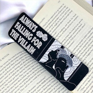 May include: A black and white bookmark featuring a stylised illustration of a person sleeping. The bookmark has white text that reads "Always Falling for the Villain".