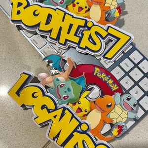 K&ouml;nnte beinhalten: Zwei mehrschichtige Tortenaufs&auml;tze mit Pok&eacute;mon-Charakteren und den Texten "BODHI IS 7" und "LOGAN IS 8". Die Aufs&auml;tze zeigen Pikachu, Glumanda, Bisasam, Schiggy und Glurak, mit einem roten Pok&eacute;mon-Logo.