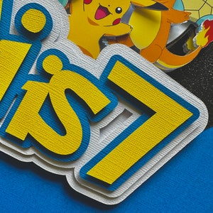 K&ouml;nnte beinhalten: Mehrschichtige Papierdekoration mit dem Text "Happy 7" in Gelb und Blau, vor blauem Hintergrund. Die Dekoration zeigt Bilder von Pikachu, Glumanda und anderen Pok&eacute;mon-Charakteren.