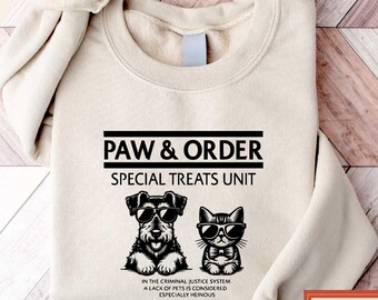 May include: Sand-colored sweatshirt with the text "PAW & ORDER SPECIAL TREATS UNIT" and a graphic of a dog and cat wearing sunglasses. The sweatshirt also has the text "IN THE CRIMINAL JUSTICE SYSTEM A LACK OF PETS IS CONSIDERED ESPECIALLY HEINOUS."