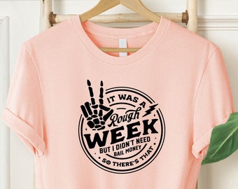 May include: A pink t-shirt with a black graphic that says "It was a rough week but I didn't need bail money so there's that."