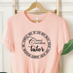May include: A pink t-shirt with a black circle design that says "Classical Conversations Tutor" with a list of subjects around the circle.