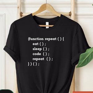 May include: Black t-shirt with white text that reads: "(function repeat () { eat (); sleep (); code (); repeat (); })();"