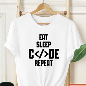 May include: White t-shirt with black text that reads "Eat Sleep Code Repeat".