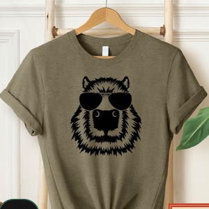 May include: A green t-shirt with a black graphic of an animal wearing sunglasses. The animal has a furry face and a long snout.