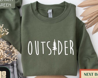 May include: A military green sweatshirt with the word "OUTSIDER" printed in white with a small pine tree graphic in the middle of the word.