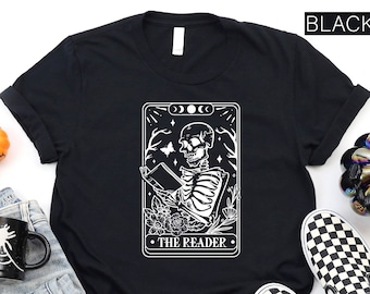 May include: Black t-shirt with a white illustration of a skeleton reading a book. The illustration is in the style of a tarot card and says "The Reader" at the bottom.