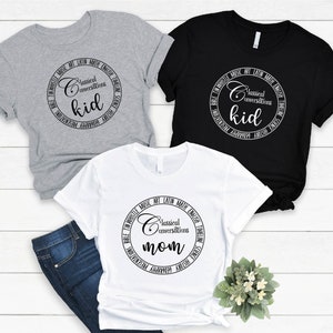May include: Three t-shirts with a circular design featuring the text "Classical Conversations" and the words "kid" and "mom". The shirts are in grey, black, and white.