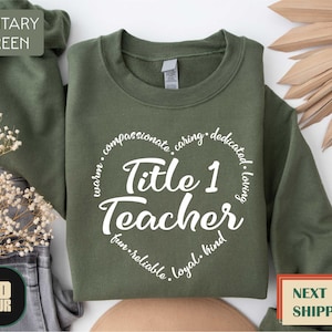 May include: A military green sweatshirt with a white circle design that says "Title 1 Teacher" and lists positive adjectives around the circle.