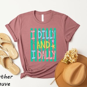 a pink t-shirt with a colorful graphic, a pair of beige flip-flops, a tan hat, and some dried flowers, all arranged on a white background.