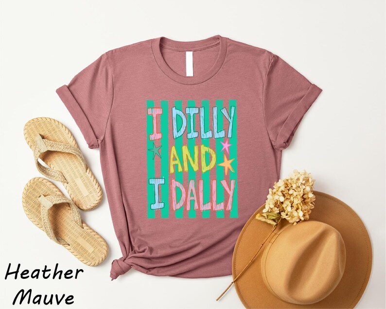 a pink t-shirt with a colorful graphic, a pair of beige flip-flops, a tan hat, and some dried flowers, all arranged on a white background.