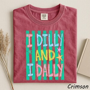 A red t-shirt with a colorful graphic design featuring the text "I Dilly and I Dally" in a playful font.