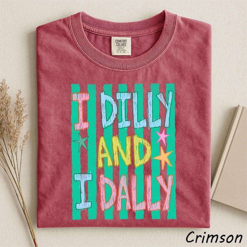 A red t-shirt with a colorful graphic design featuring the text "I Dilly and I Dally" in a playful font.