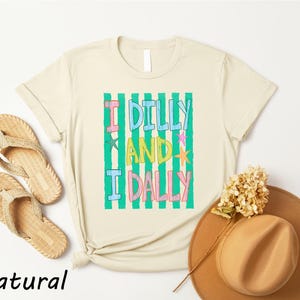 a casual outfit consisting of a beige t-shirt with a colorful graphic, a pair of beige flip-flops, a brown hat, and a dried flower.