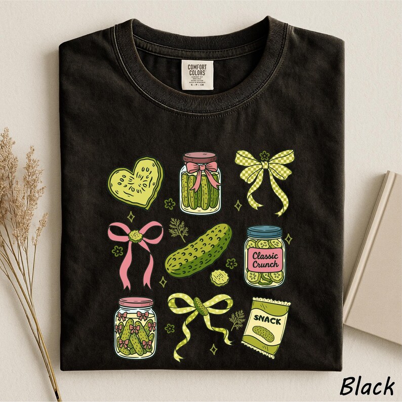 A black t-shirt with a graphic design featuring various pickle jars, a heart, a bow, a jar of cookies, and a bag of chips.