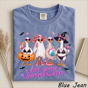 May include: A blue jean colored t-shirt featuring a graphic of four geese dressed in summer and Halloween costumes. The geese wear sunglasses, swimsuits, and hats, with a pumpkin float, beach ball, and cocktails. Text reads hot goose Summerween.