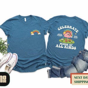 May include: A teal blue t-shirt with a rainbow and sun graphic on the front and the text "Celebrate Minds of All Kinds" with a cartoon brain character on the back.