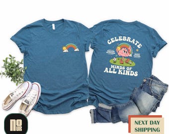 May include: A teal blue t-shirt with a rainbow and sun graphic on the front and the text "Celebrate Minds of All Kinds" with a cartoon brain character on the back.