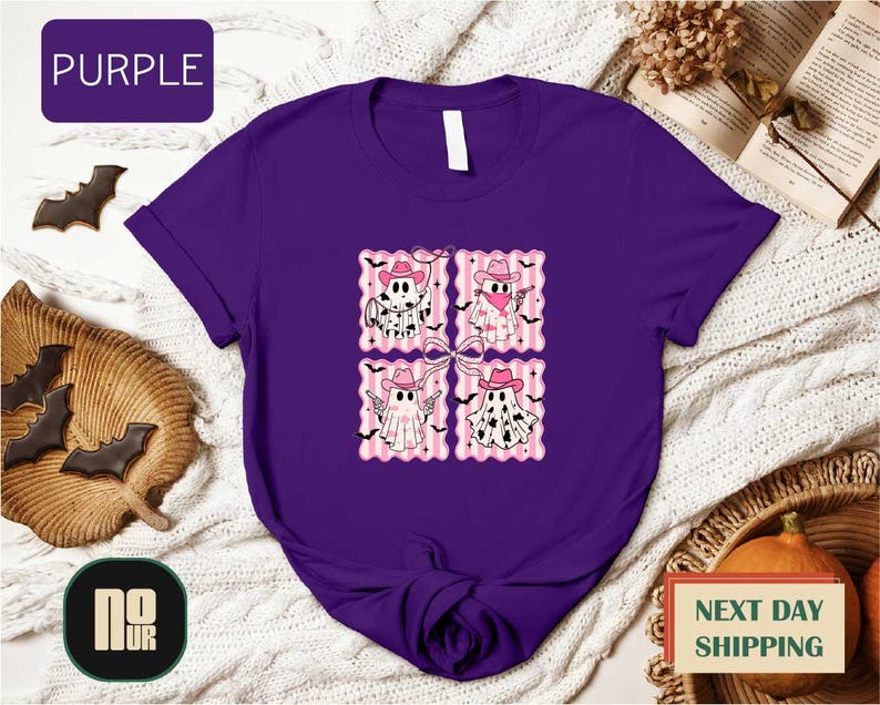 a purple t-shirt with a graphic design of four cartoon-style ghost characters, each wearing a pink hat and bow tie. The t-shirt is displayed on a white background, surrounded by various Halloween-themed items such as bats, pumpkins, and a book.