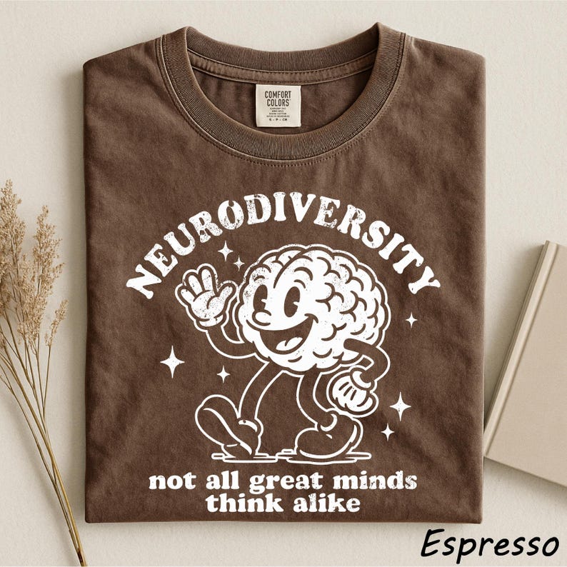 A brown t-shirt with a white graphic design depicting a smiling brain character and the text "Neurodiversity not all great minds think alike" printed on it.