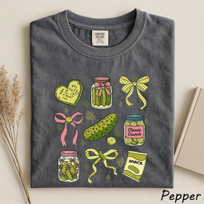 a gray t-shirt with a variety of colorful illustrations, including jars of pickles, a heart, a bow, a jar of chips, and a bag of candy.