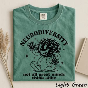 A green t-shirt with a graphic design of a smiling brain character and text that reads "Neurodiversity not all great minds think alike".