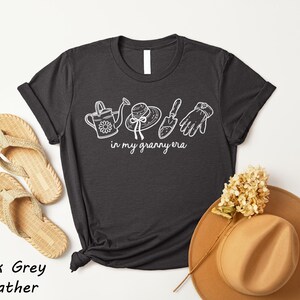 a black t-shirt with white text and illustrations, a pair of beige flip-flops, a tan hat, and a dried flower, all arranged on a white background.