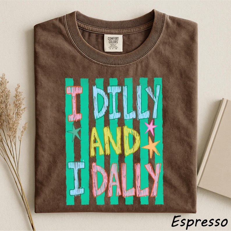 A brown t-shirt with a colorful graphic design featuring the text "I Dilly and I Dally" in a playful font.