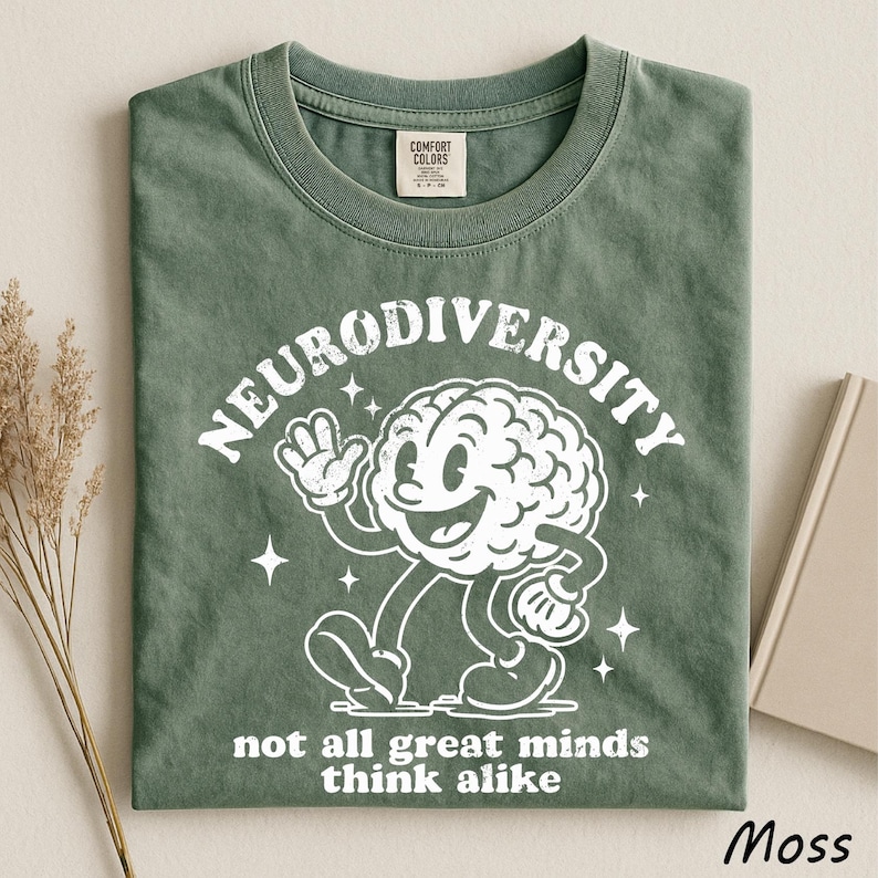 A green t-shirt with a white graphic design depicting a smiling brain character and the text "Neurodiversity not all great minds think alike" printed on it.