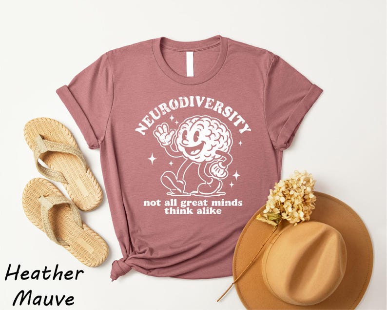 a pink t-shirt with a white graphic of a brain and the text "Neurodiversity" and "not all great minds think alike" printed on it, along with a pair of beige flip-flops and a beige hat.