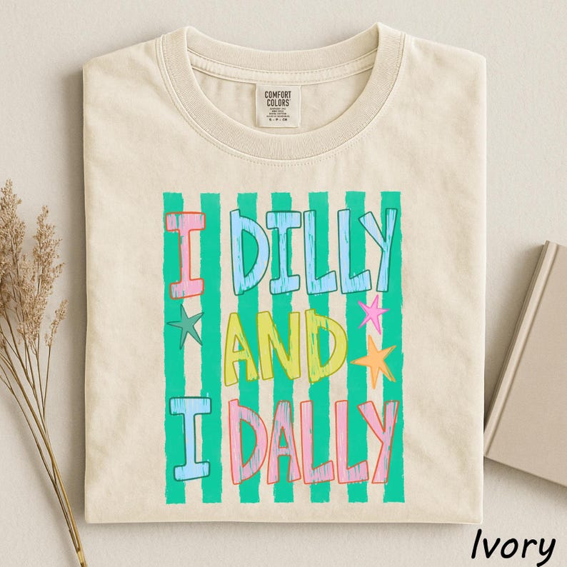 A beige t-shirt with a colorful graphic design featuring the text "I Dilly and I Dally" in a playful font.