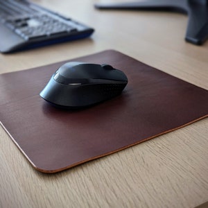 May include: A dark brown leather mouse mat with a black wireless mouse on top.