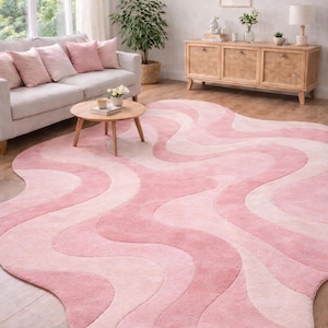 Puede incluir: Una gran alfombra con un patrón ondulado en tonos rosa y crema domina la habitación. El diseño de la alfombra presenta formas orgánicas fluidas, creando una estética suave y acogedora. La alfombra está colocada sobre un suelo de madera.