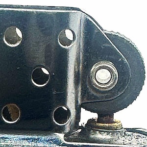 May include: A metallic lighter insert featuring a chimney with five circular ventilation holes on each side and a textured flint wheel mechanism. The component is constructed from polished steel and includes a central rivet securing the flint wheel.
