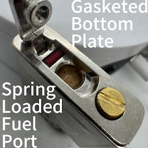 May include: A metallic lighter insert featuring a Gasketed Bottom Plate and a Spring Loaded Fuel Port. The component includes a brass-colored screw, a small red rectangular element, and a central circular opening containing fibrous material.