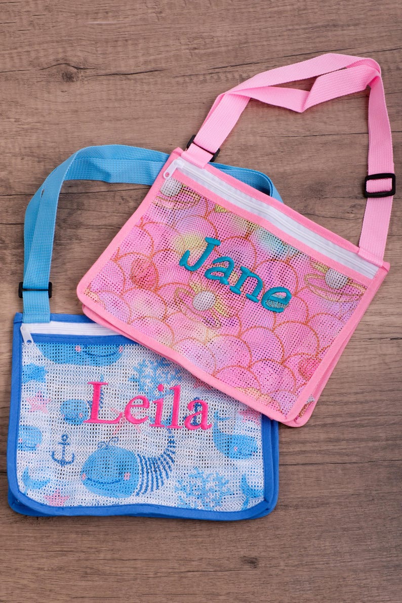 May include: Two mesh crossbody bags. One is pink with a floral pattern and the name "Jane" in teal. The other is blue with a whale and anchor pattern and the name "Leila" in pink. Both have adjustable straps.