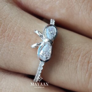 以下が含まれることがあります： ユニークなデザインのシルバーリングのクローズアップ。リングは、2つのペアシェイプの宝石と、小さな石で飾られたバンドが特徴です。リングは人の指にあります。「MAYAAN fine jewelry」のブランド名が見えます。