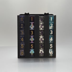 May include: A black acrylic dice tower with six columns of dice. Each column has a different color and pattern of dice with numbers 1 through 6. The dice are made of clear acrylic with a purple and gold color scheme.