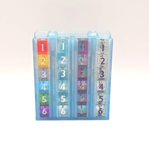May include: A clear, blue plastic number cube with six columns of dice. Each die has a different color and glitter. The numbers 1 through 6 are visible on each die. The dice are arranged in a vertical row.