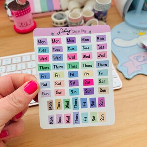 May include: A sheet of colorful stickers with the days of the week labeled in black text. The stickers are arranged in a grid pattern and are perfect for planning and organizing.