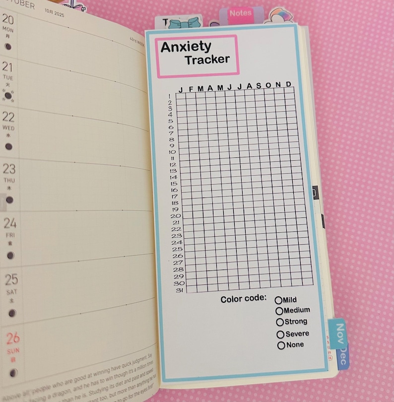 May include: A planner insert with the text "Anxiety Tracker" in a pink and blue frame. The insert features a grid for tracking anxiety levels throughout the year, with a color code for different intensities. The planner is open to the October 2025 page.