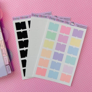May include: Three sticker sheets with the text "Daisy Sticker City" and "Daisy Sticker C". One sheet has black stickers, one has white stickers, and one has pastel-colored stickers. The stickers are in the shape of the letter "M".