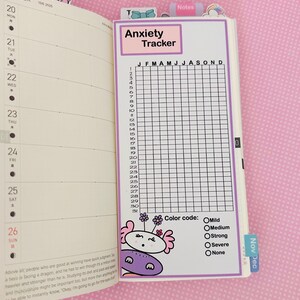 May include: Anxiety tracker insert for a planner, featuring a grid for daily tracking from January to December. The insert has a color code for anxiety levels: mild, medium, strong, severe, and none. A cute cartoon character is at the bottom.