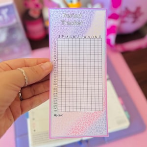 May include: A rectangular period tracker card featuring a pastel gradient background with a subtle leopard print pattern. The card includes a grid with columns for months J through D and rows numbered 1 through 31, with a section for Notes at the bottom.