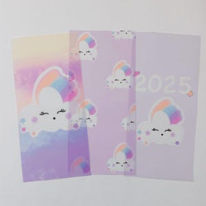 May include: Three clear plastic sheets with a rainbow cloud design. The sheets are layered on top of each other. The top sheet has the year 2025 printed on it in white.
