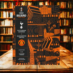 May include: A black and orange official program for the Europa League Final 2025 in Bilbao. The program features the Tottenham Hotspur versus Manchester United match details, date, time, and stadium information. The design includes the Bilbao logo and city illustrations.