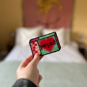 May include: A green and pink embroidered patch with a red heart and the word "perfect" in black lettering.