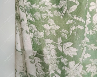 May include: Close-up of a green fabric with a white floral pattern. The fabric has a textured surface and a subtle sheen.